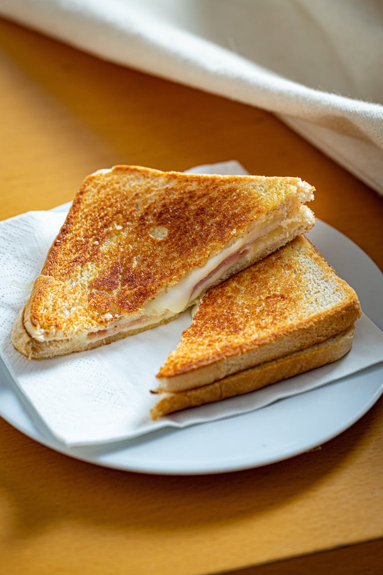 Golden brown grilled cheese sandwich on a white plate with napkin.